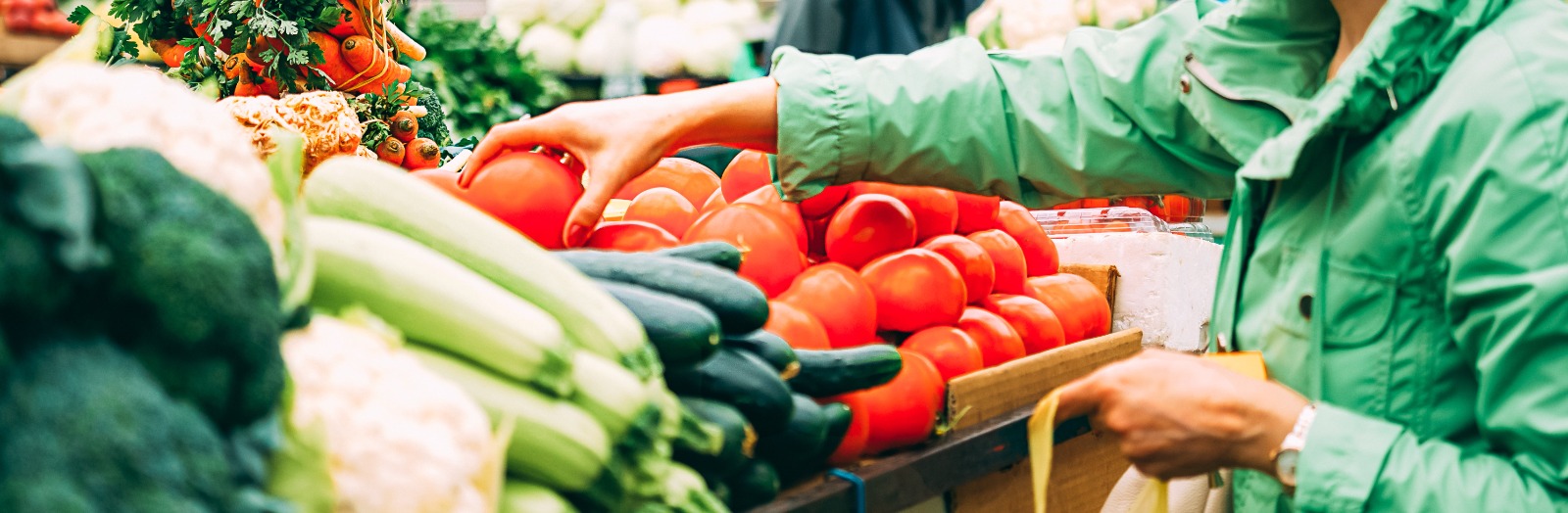 Person picking up a tomato from a vegetable stand